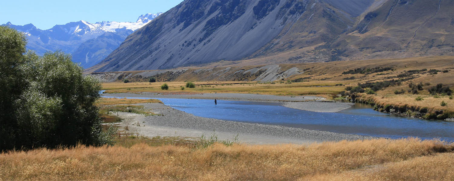 Wide panoramic view of Ahuriri River surrounded by tussock and steep snow capped mountains in the High Country, New Zealand