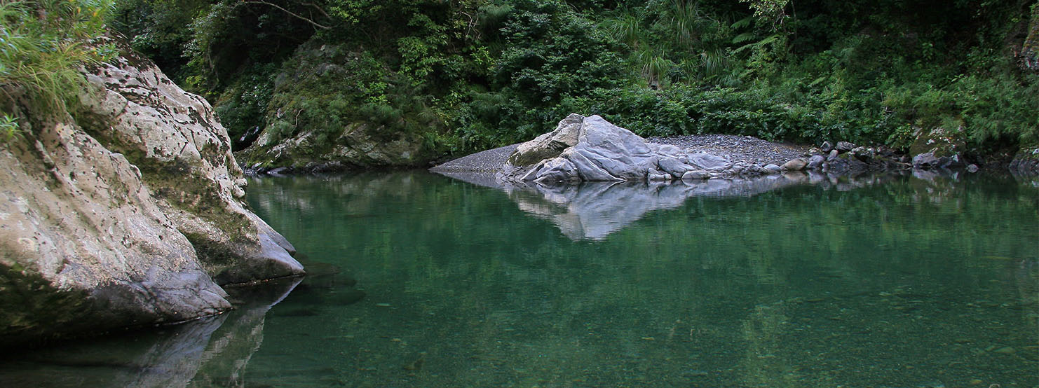Mirror like reflections of rocks and bush-clad valley on a still pool in a backcountry river, New Zealand