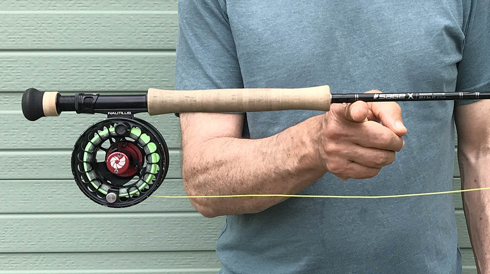 Man balancing a rod and reel on his finger in front of a pale green garage door