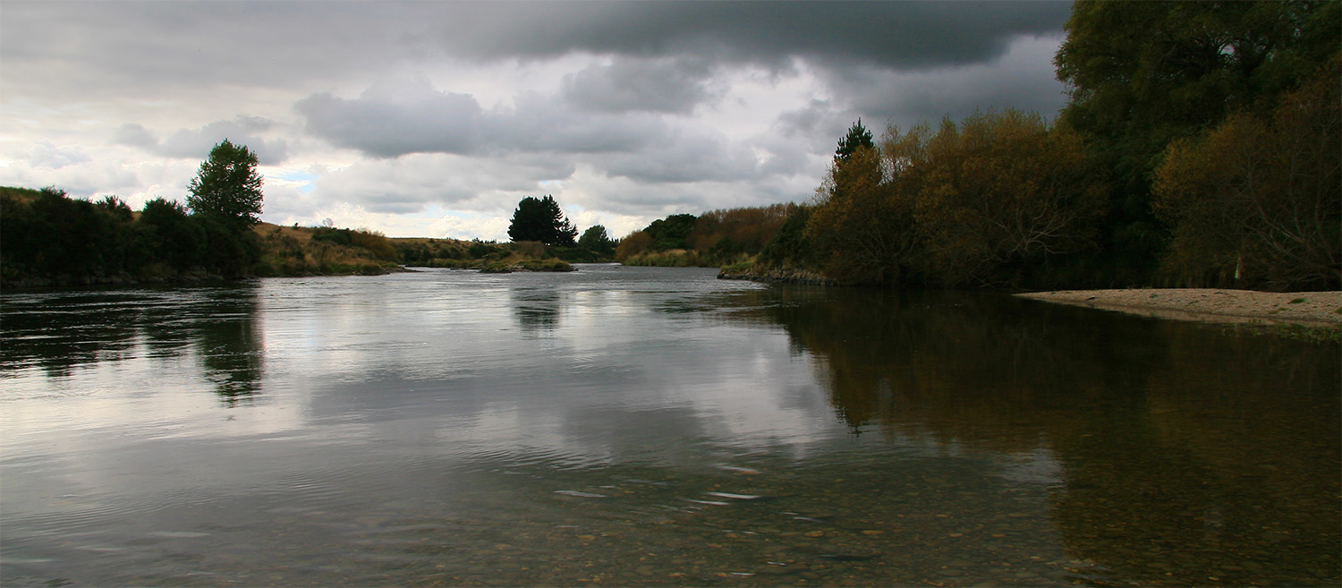 Moody river with overcast clouds reflected on the water, lower south island