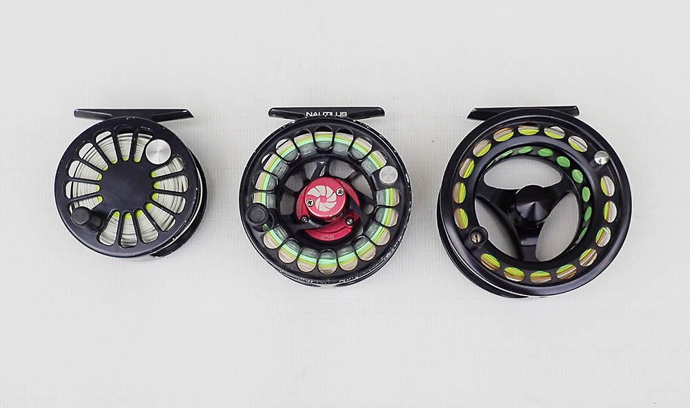 Three fly fishing reels of increasingly smaller size laid out in a row on a pale white cloth