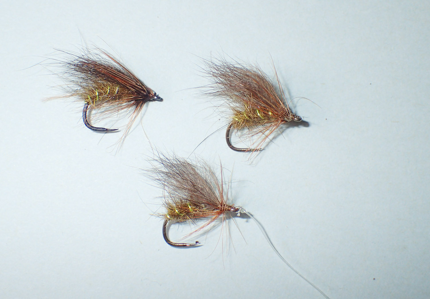 Three Possum Caddis wet flies on a pale bluish green background